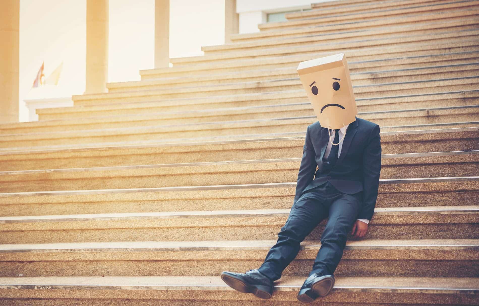 A person in a suit, embodying a Los Angeles employment attorney's struggles, sits on stairs with a paper bag donning a sad face drawn on it. Consumer Rights