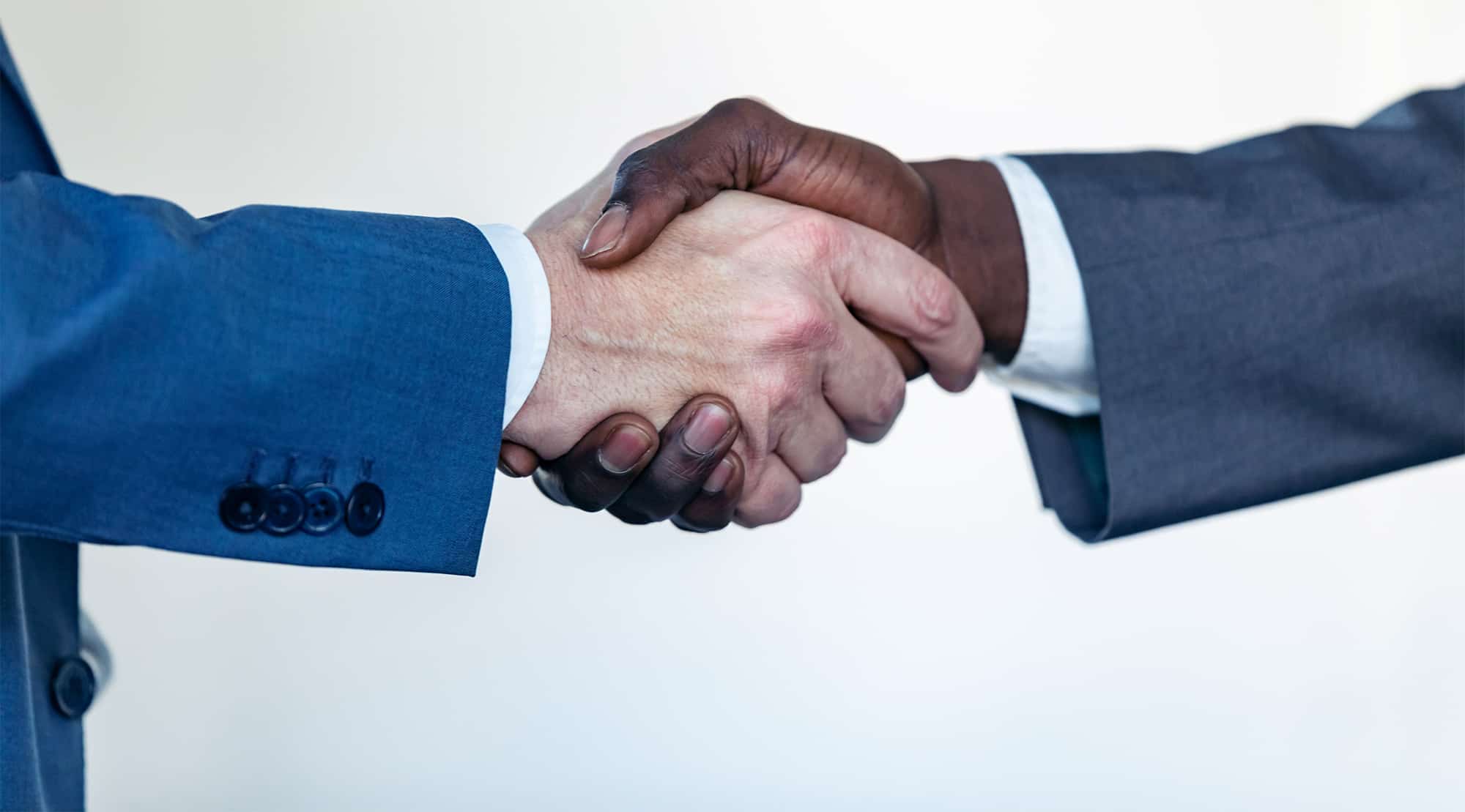 Two people in business attire are shaking hands, one wearing a blue suit and the other a dark gray suit, against a light background, reminiscent of an employment lawyer Los Angeles sealing an important deal. Consumer Rights