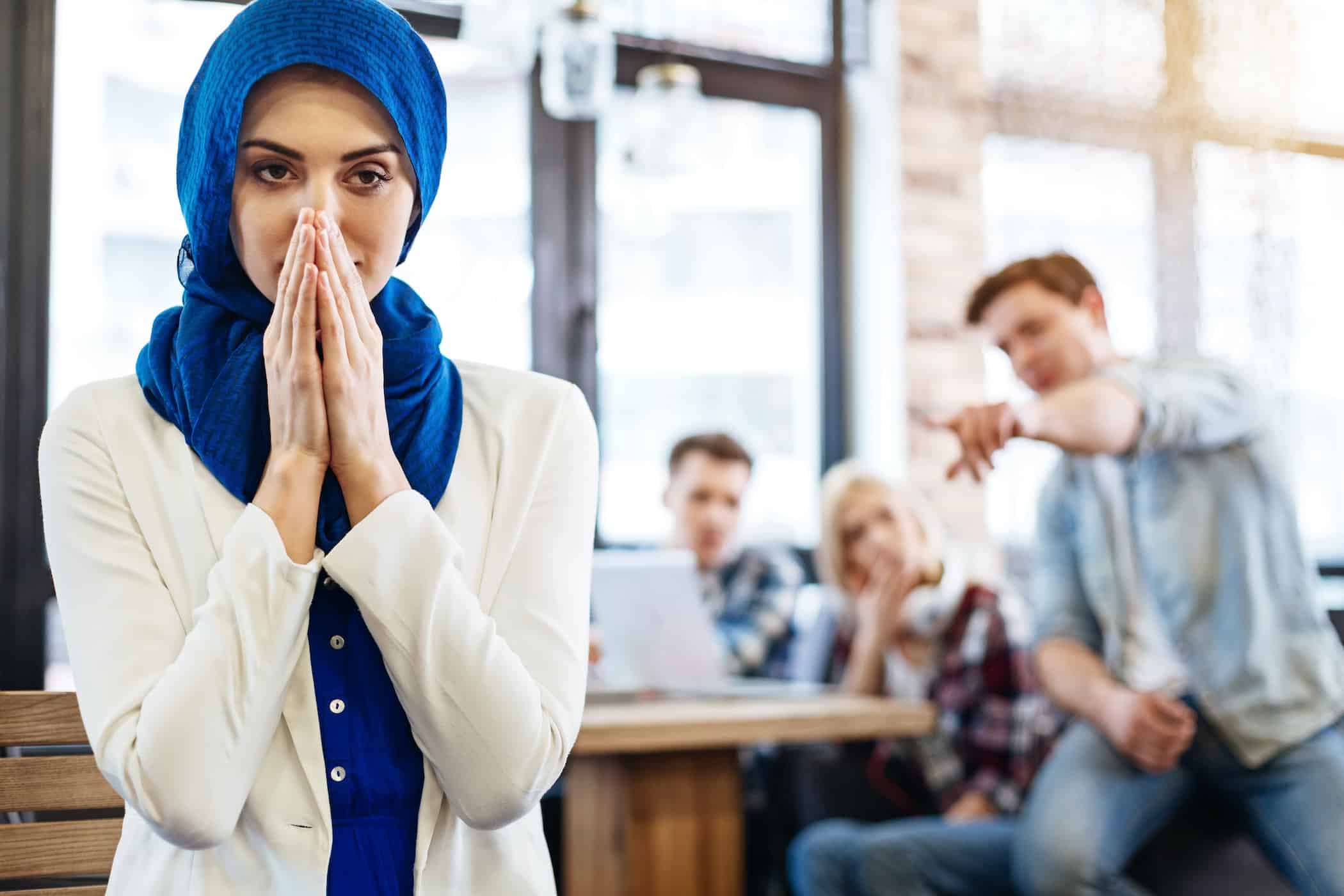 A woman in a blue hijab stands in the foreground, looking concerned. In the background, three people are talking and pointing in her direction, possibly discussing matters that require the expertise of an employment lawyer in Los Angeles.