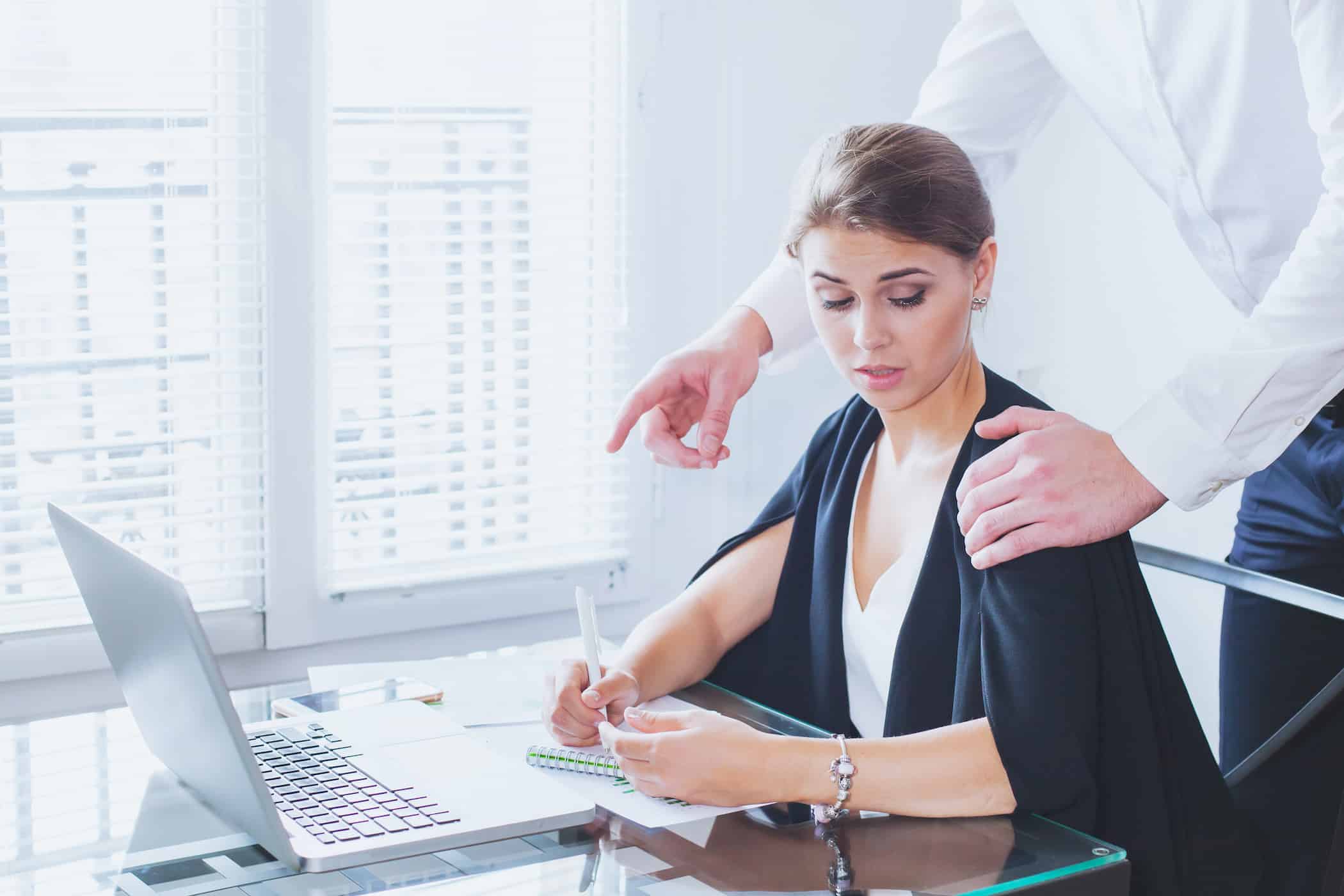 A person sitting at a desk with a laptop, looking surprised or concerned as an employment lawyer in Los Angeles stands behind, pointing at a document on the desk.