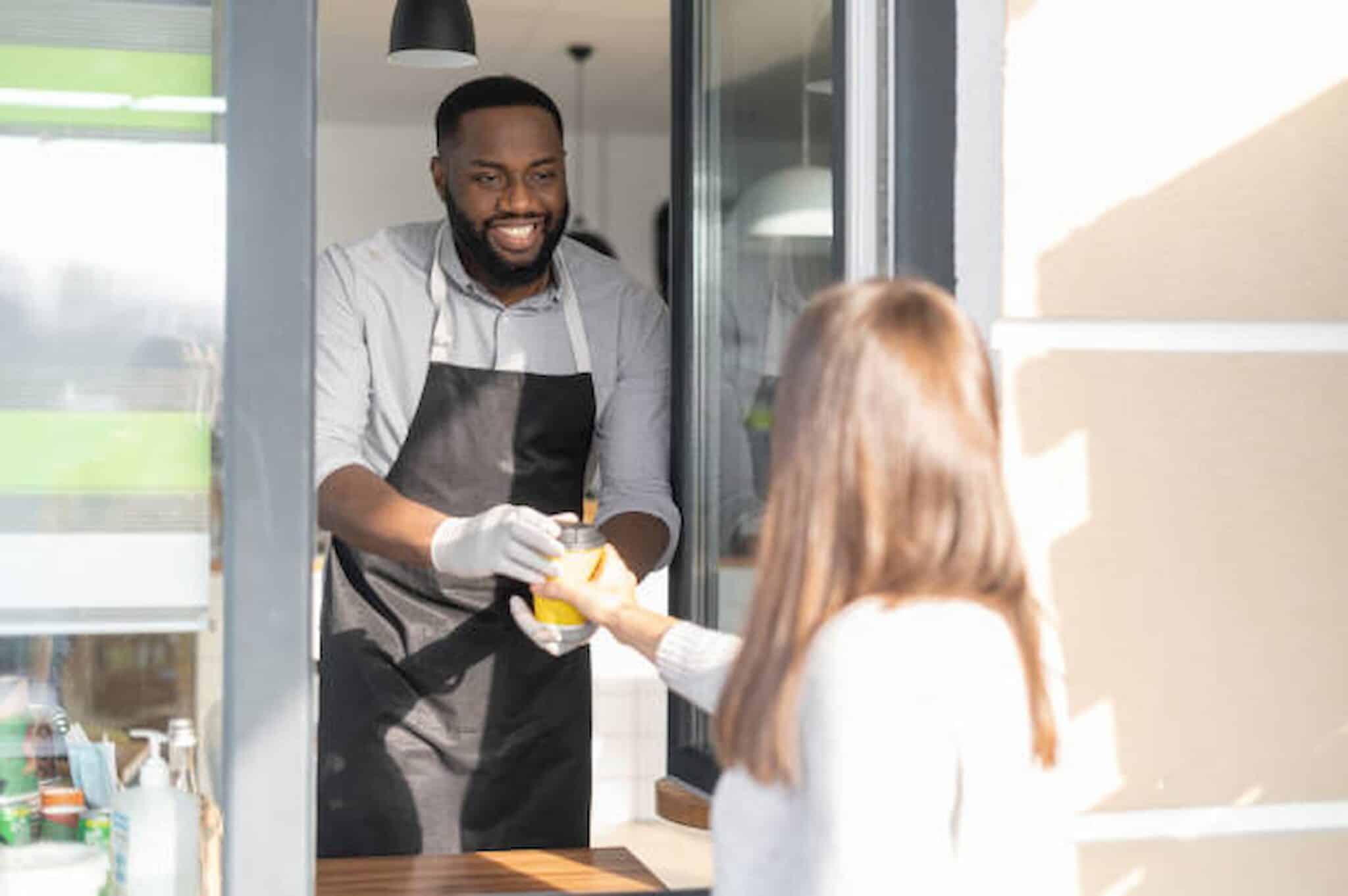 A man in an apron hands a drink to a woman through a window, reminiscent of the friendly neighborhood vibe you'll find at your local cafe. Just like an attentive Los Angeles employment attorney ensures every detail is handled with care, this moment reflects dedication and service. Employee Rights