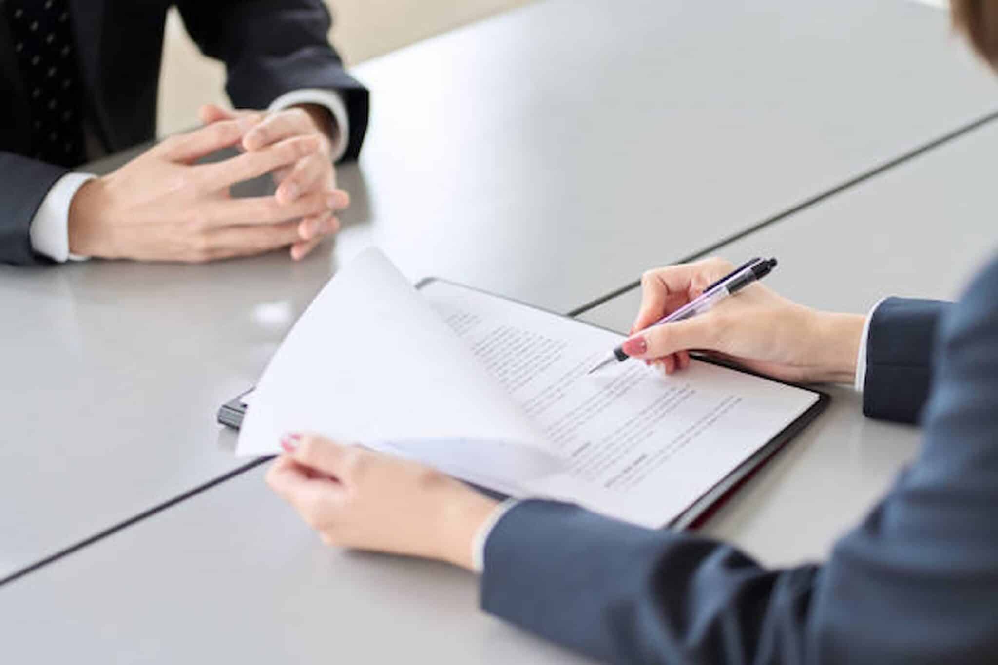 Two people in business attire sit at a table. One, perhaps an employment lawyer from Los Angeles, is writing on a document while the other has their hands clasped, suggesting a meeting or discussion. Employee Rights