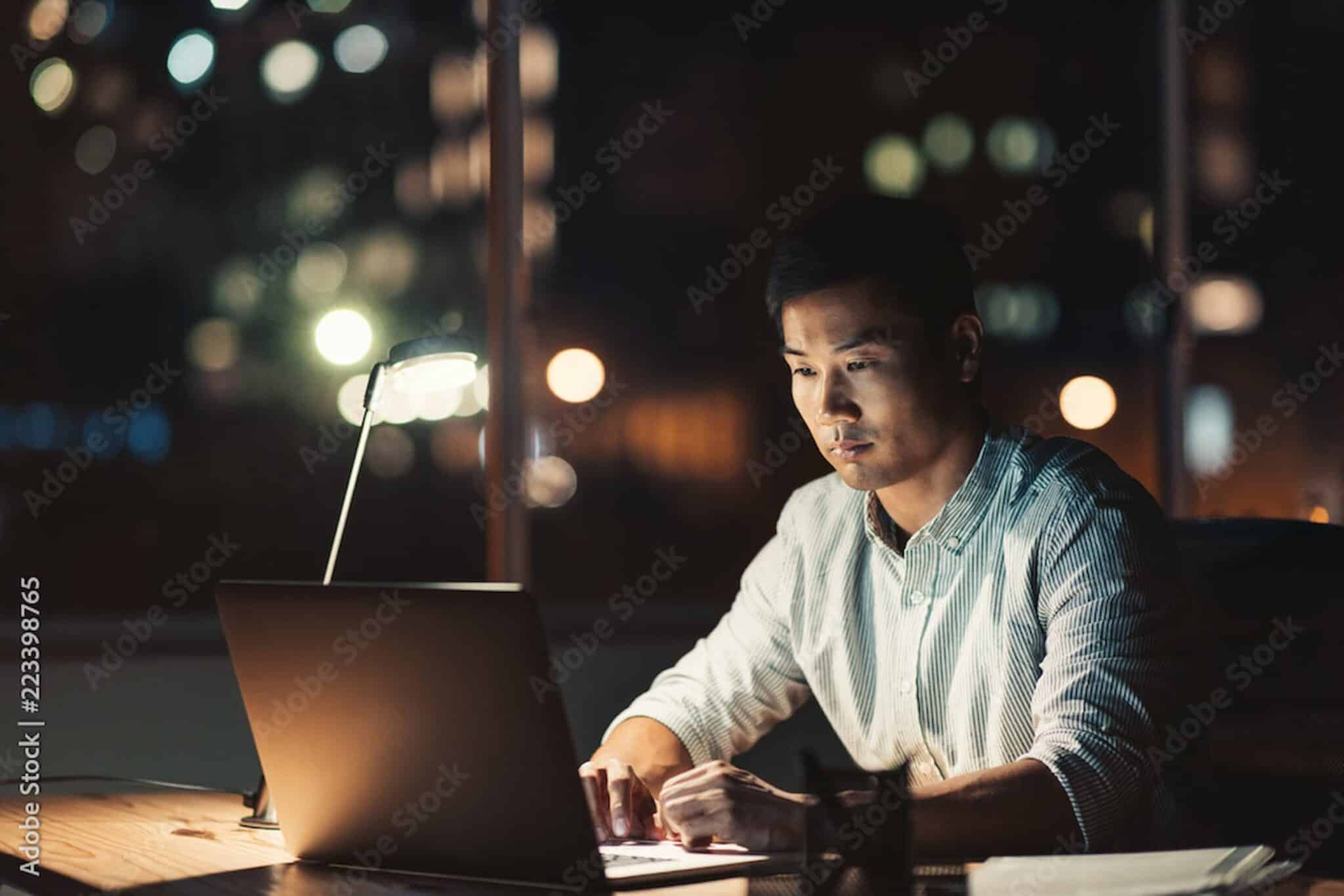 A consumer protection attorney works diligently on a laptop at a desk in a dimly lit room, with blurred city lights twinkling in the background. Employee Rights