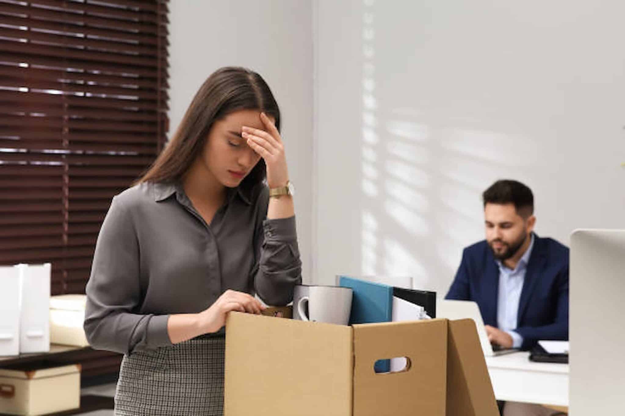 A person packing office items into a box appears upset, possibly in need of a Los Angeles employment attorney, while another person works on a computer in the background. Employee Rights
