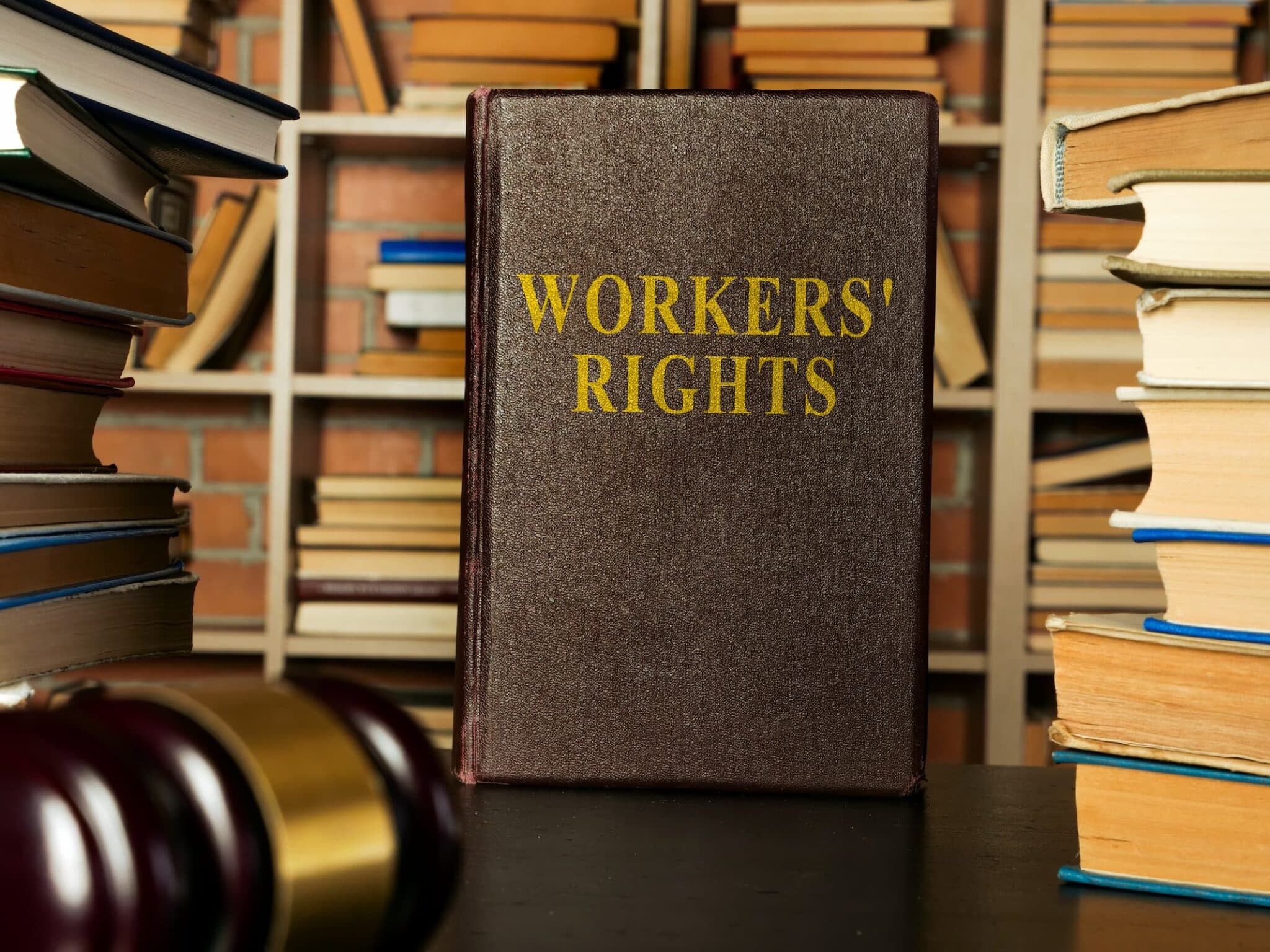 A book titled "Workers' Rights" stands on a table surrounded by other books, with a gavel nearby—an essential read for any Los Angeles employment attorney. Employee Rights