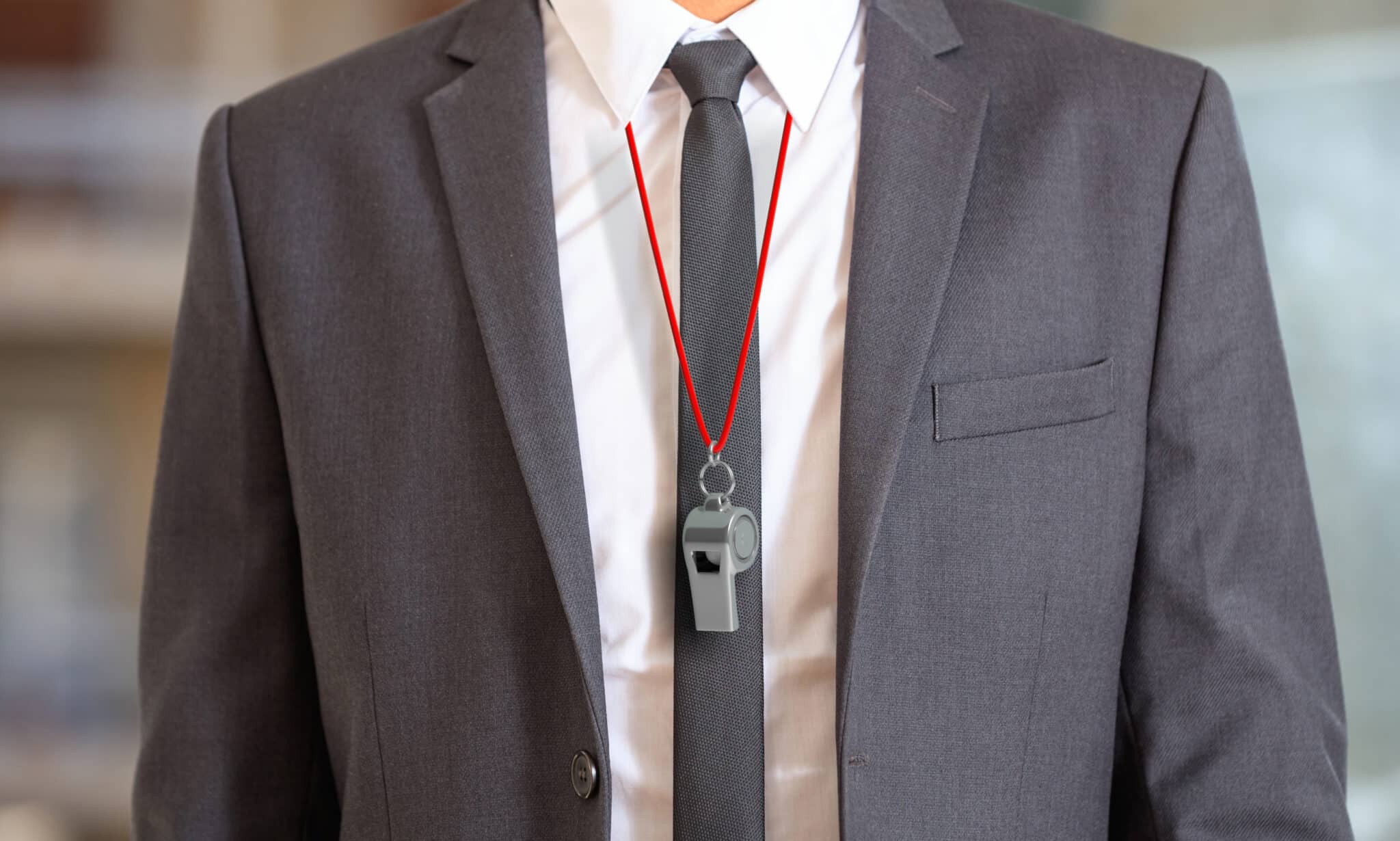 A person in a gray suit and black tie, resembling a Los Angeles employment attorney, is wearing a whistle on a red lanyard around their neck. Employee Rights>Retaliation