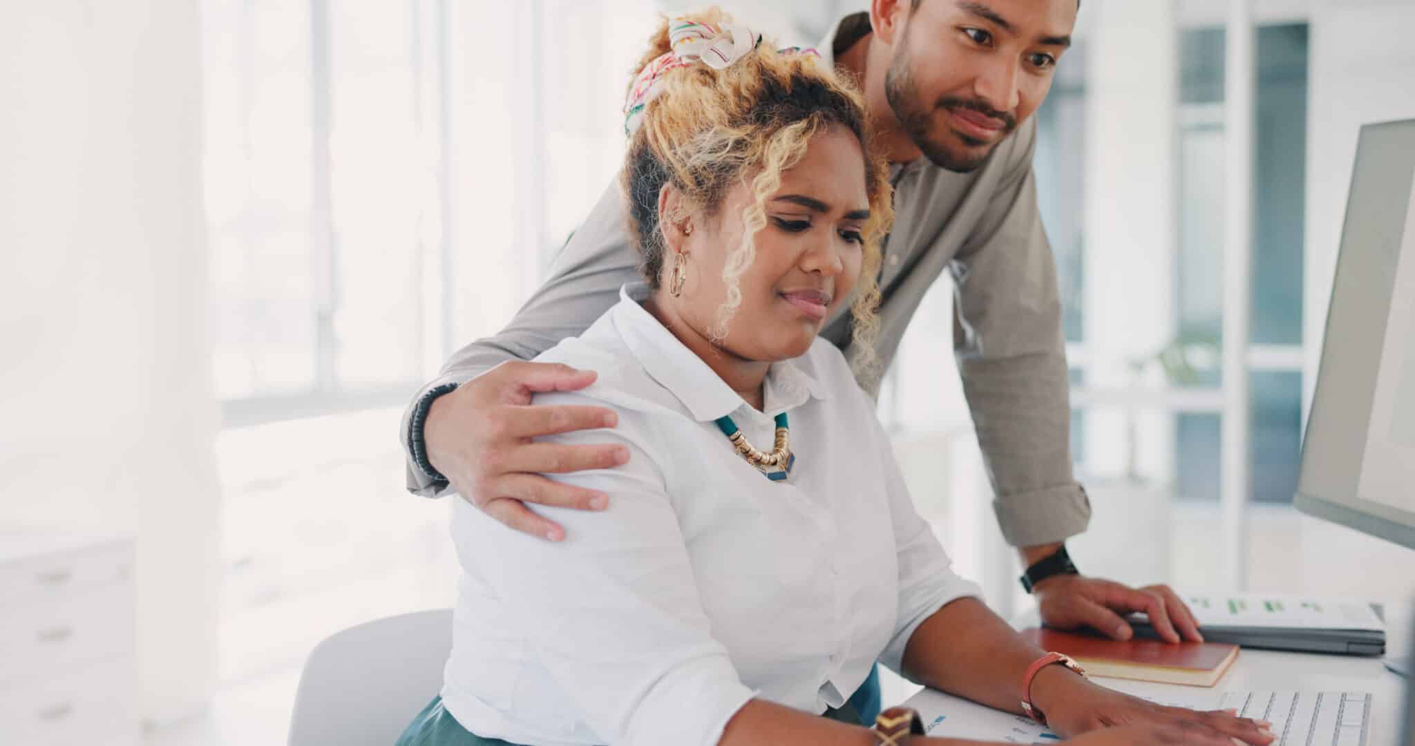 A man stands beside a woman working on a computer, his arm around her shoulder, as they discuss legal strategies with their Los Angeles employment attorney. Employee Rights>Hostile Work Environment