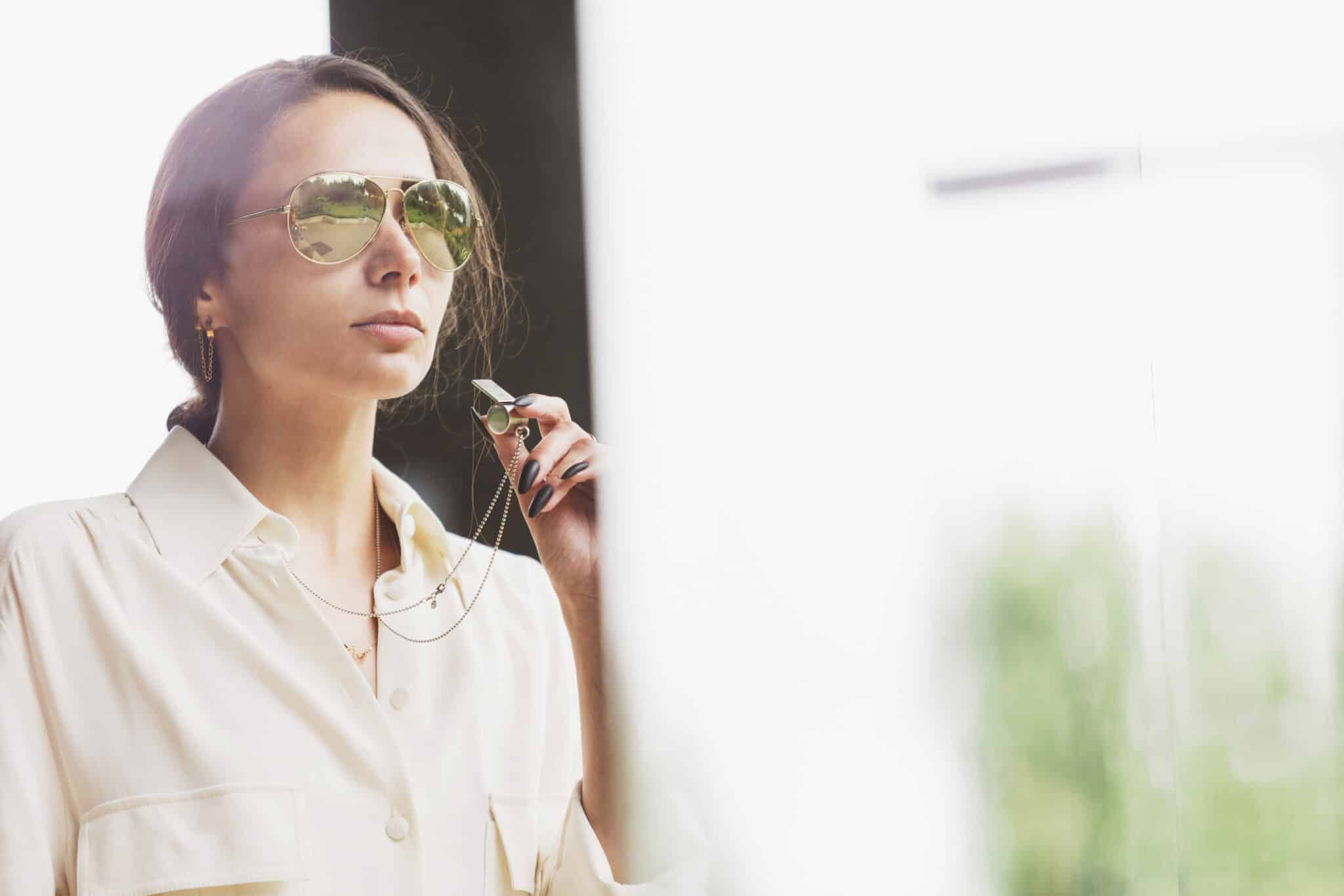 A person wearing sunglasses and a white shirt holds sunglasses by their mouth, looking ahead with a neutral expression, perhaps pondering their next move as a Los Angeles employment attorney. Employee Rights>Retaliation