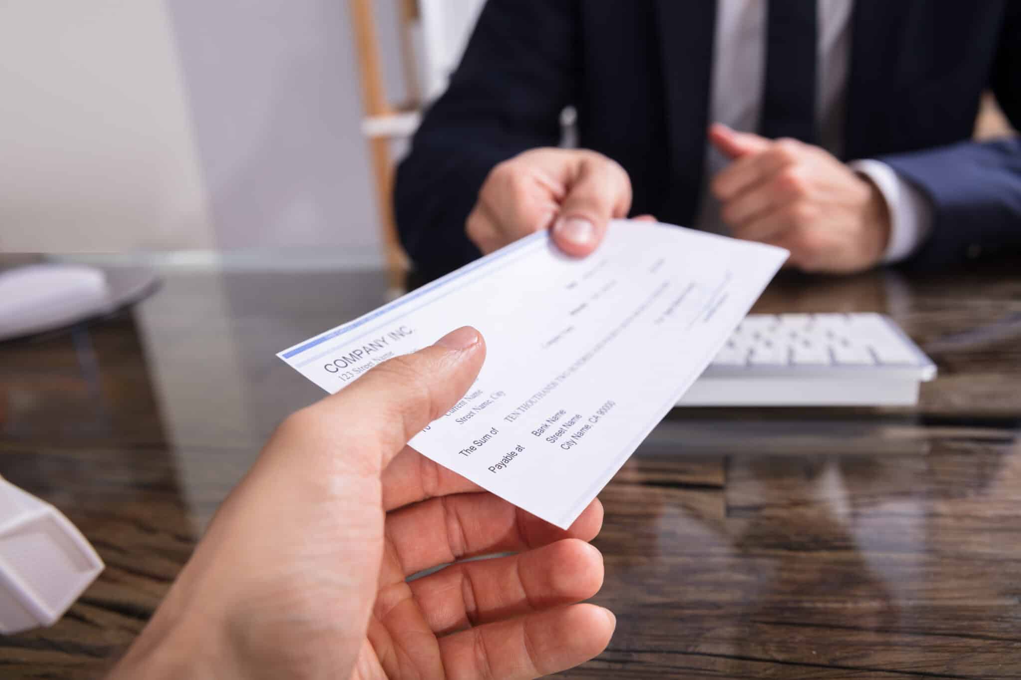 A person hands over a check to another individual sitting at a desk, consulting with an employment lawyer in Los Angeles. Employment Law