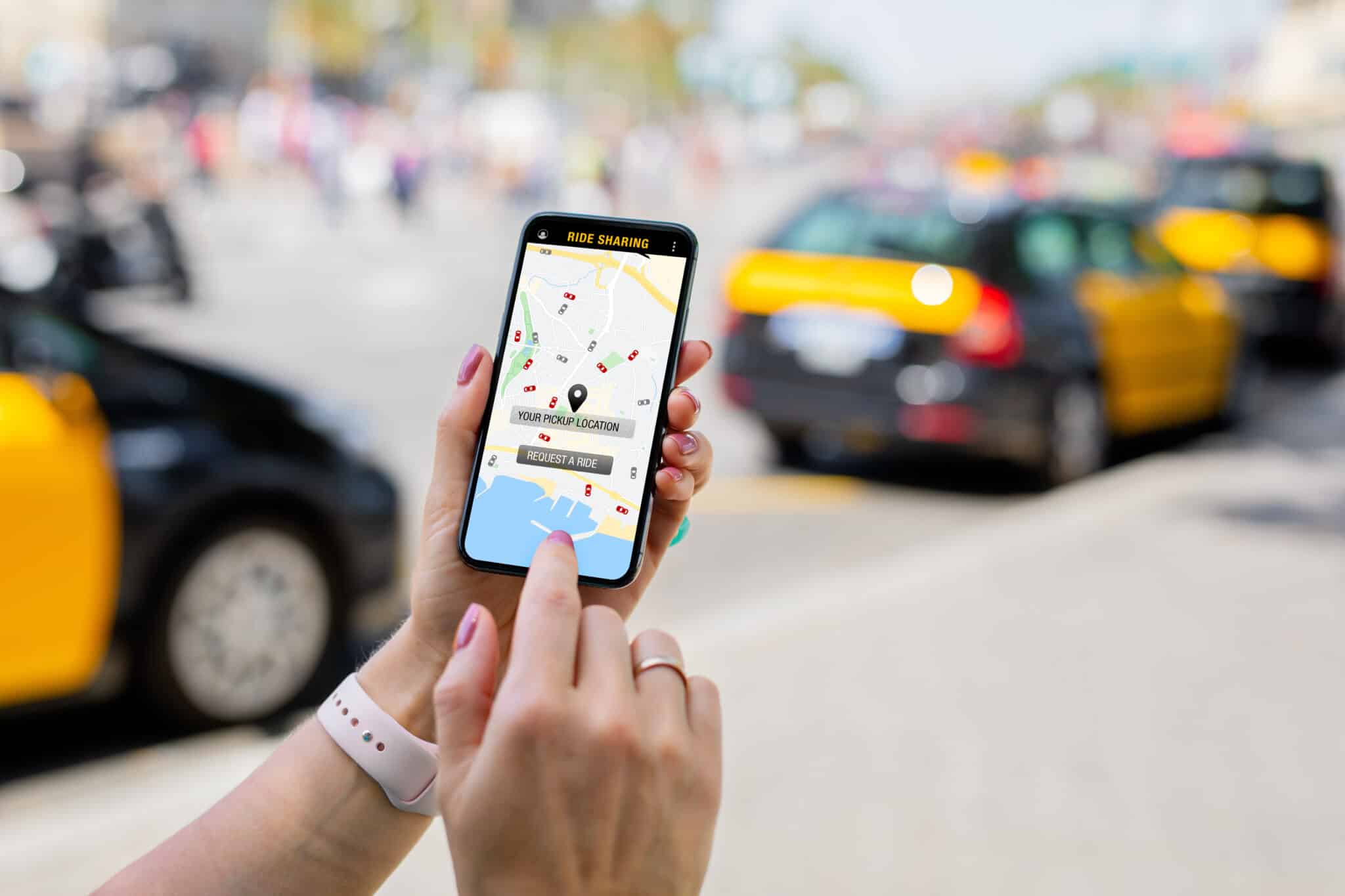Amidst the bustling street with yellow and black taxis in the background, a person uses a ride-sharing app on their smartphone. Just like finding an employment lawyer in Los Angeles, technology seamlessly connects us to what we need when navigating life's busy avenues. Employee Rights>Unpaid Wages