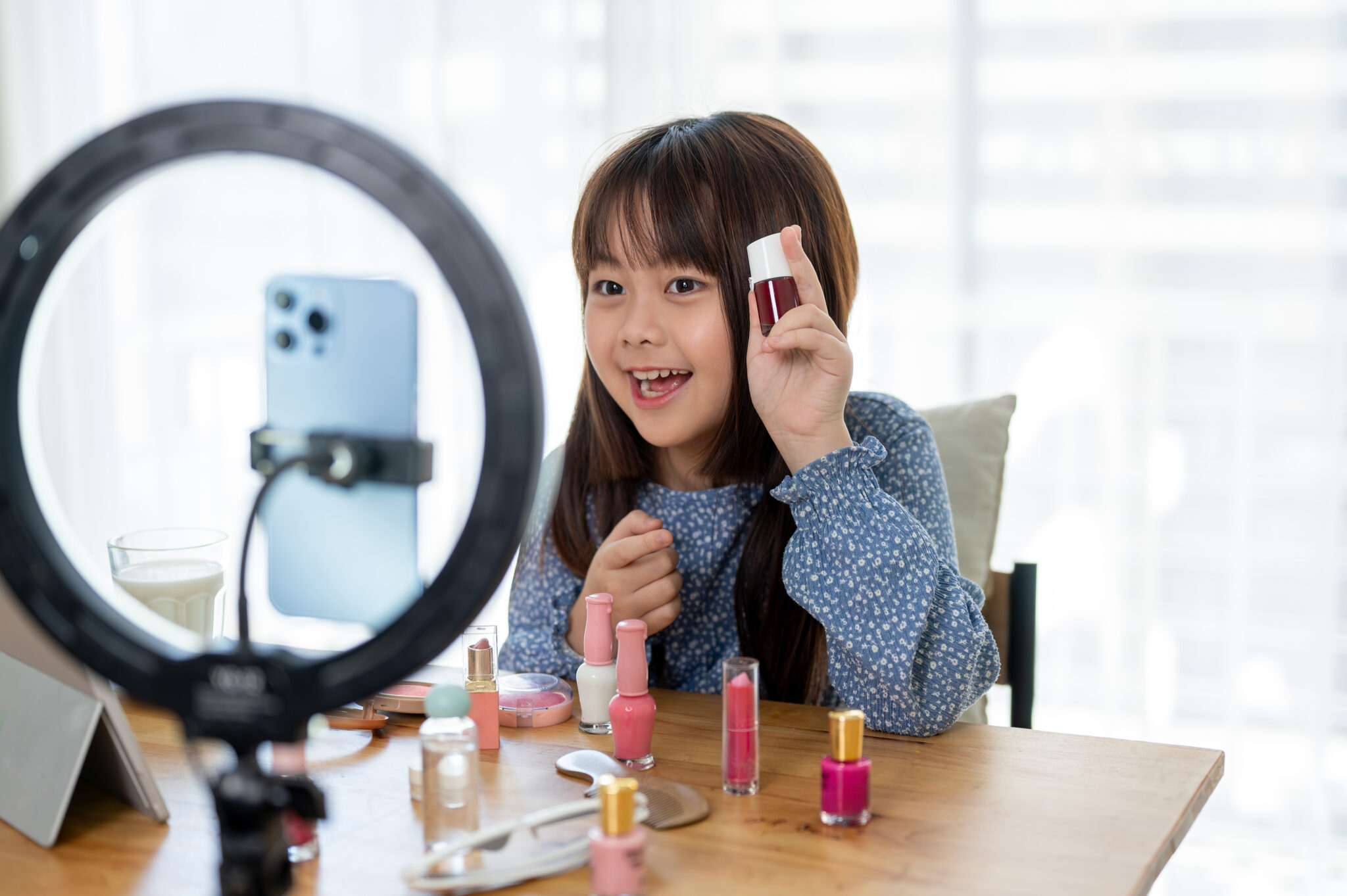 A young girl records a video showcasing nail polish, sitting at a table with various bottles and using a smartphone with a ring light, much like an aspiring consumer protection attorney preparing her case in style. Employee Rights