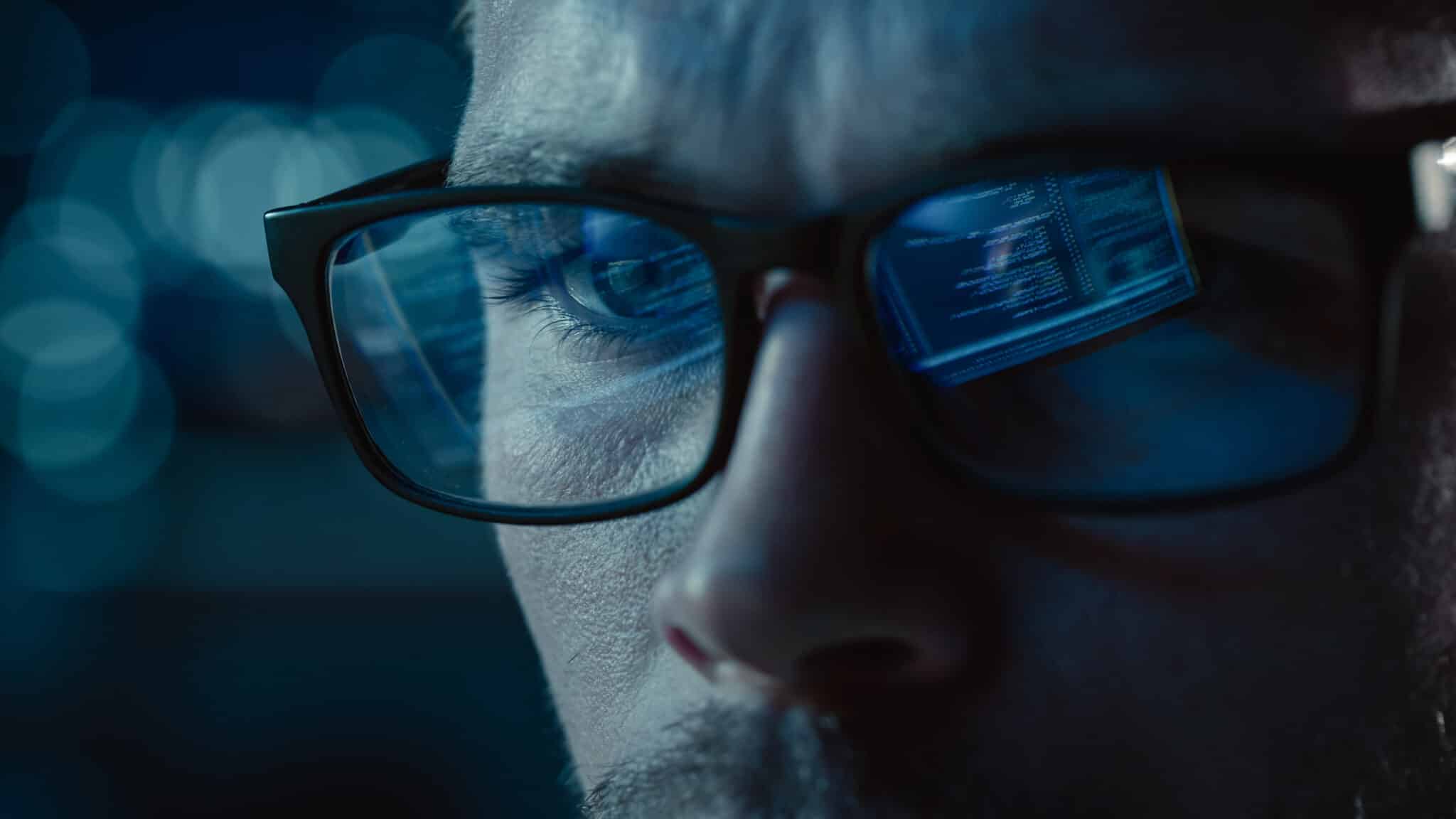Close-up of a person with glasses, reflecting computer code on the lenses. The background is blurred with blue tones, reminiscent of a digital realm, akin to where an employment lawyer in Los Angeles might sift through data in pursuit of justice.