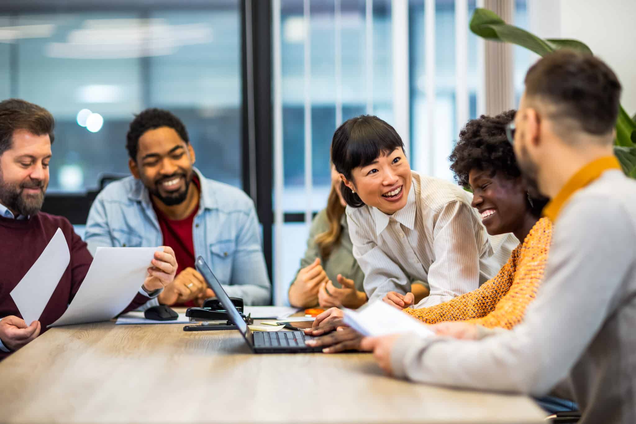 A group of people, including a Los Angeles employment attorney, sit around a table, smiling and discussing legal cases with papers and a laptop in front of them.
